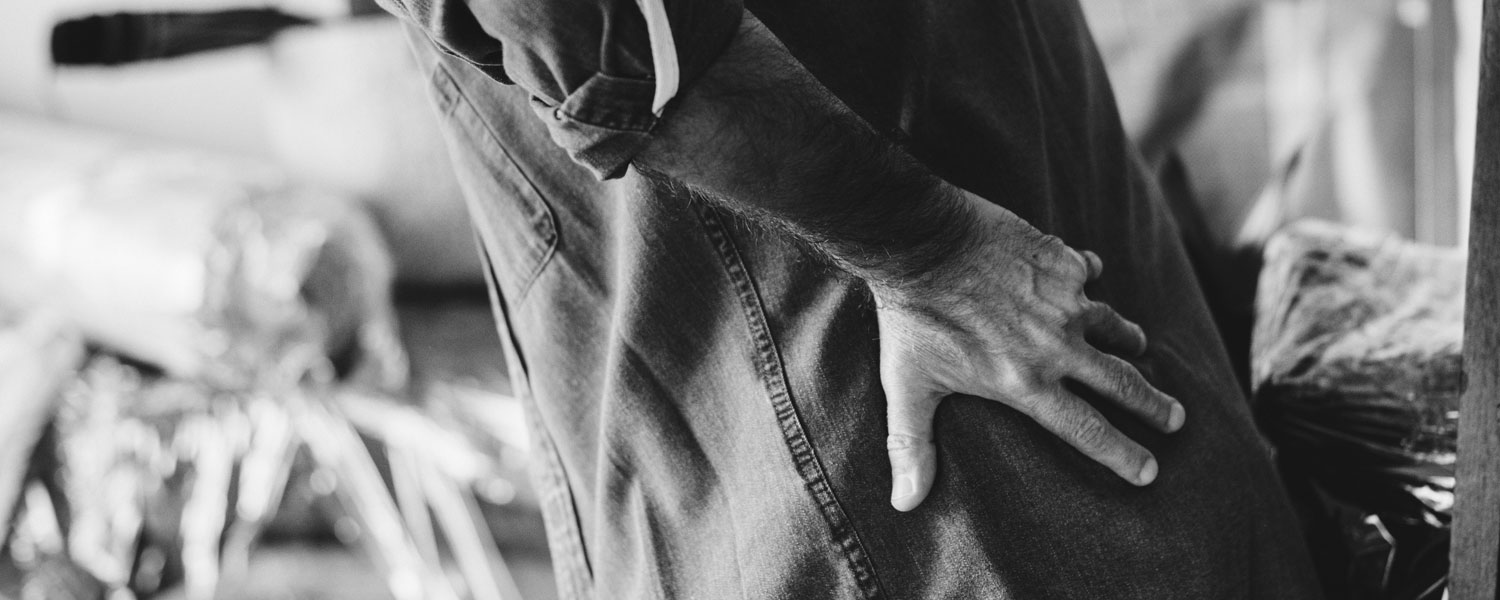 Black-and-white photo of man grabbing his upper thigh in attempt to relieve pain.