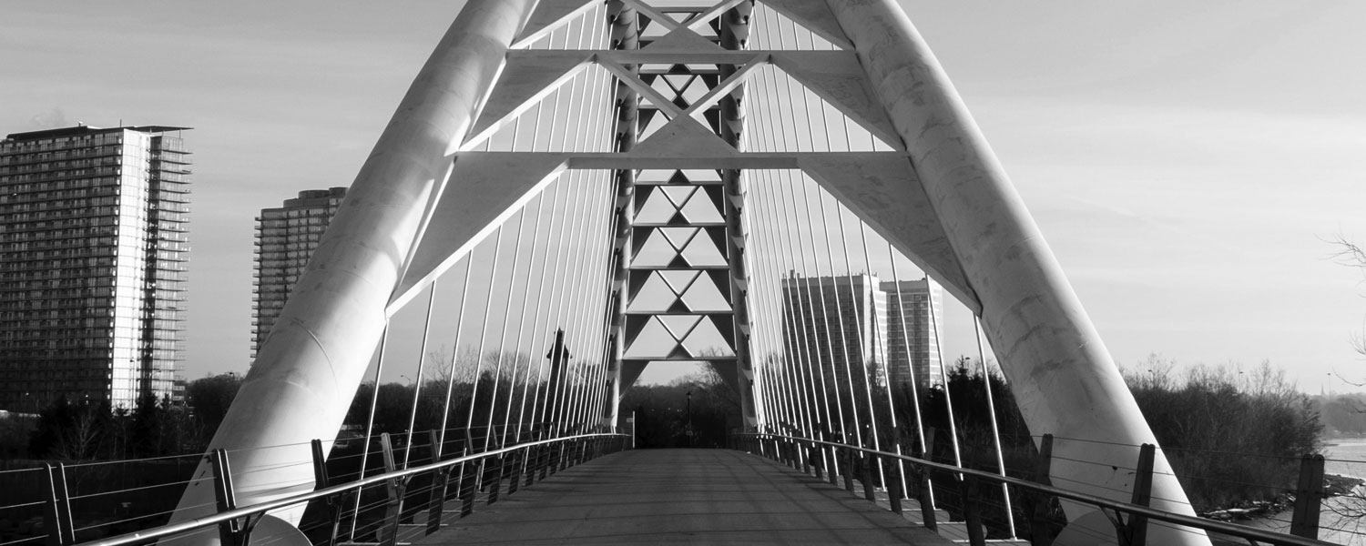 Black-and-white photo of Humber Bay Arch bridge in Toronto with 4 tall condominium buildings in the background.